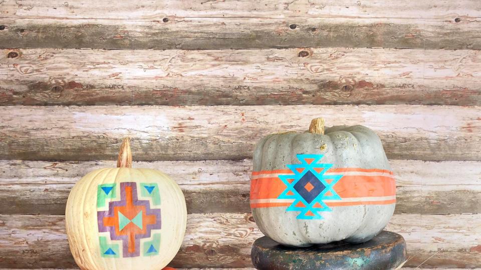 pumpkins decorated to look like pendleton blankets displayed with wool blankets, rustic chest, in front of log cabin wall