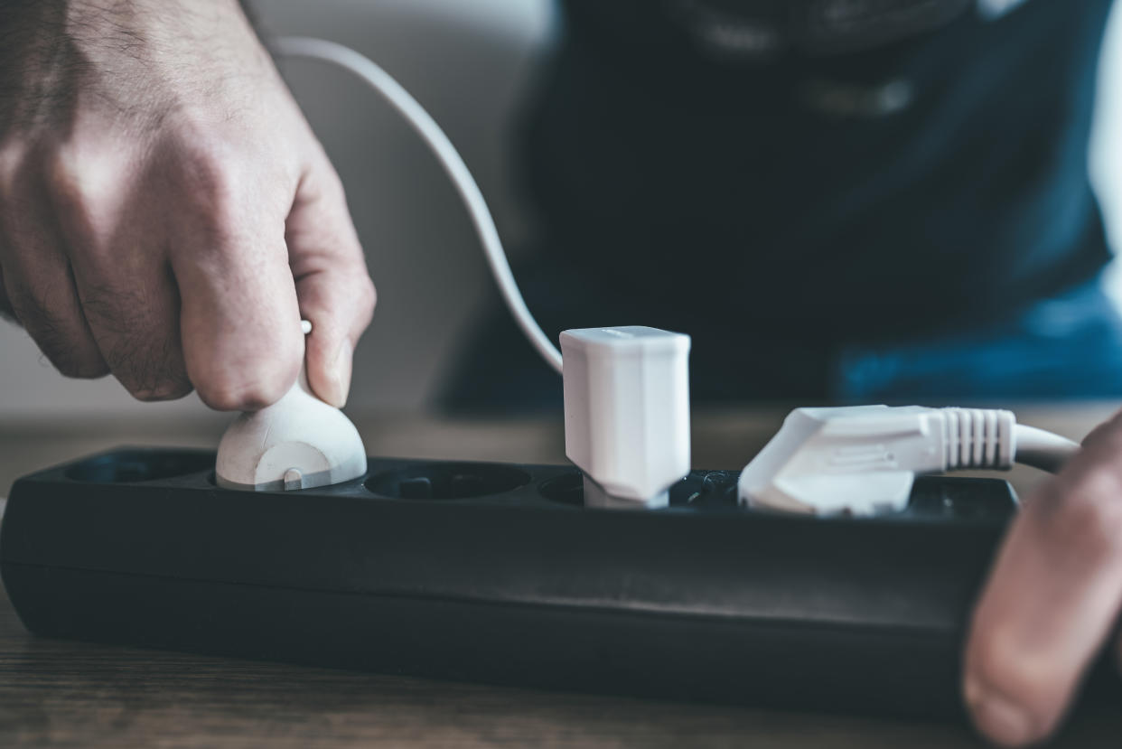 close-up of hand plugging power cable into power strip outlet