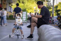 A man and girl wearing face masks cool off in the shade on an unseasonably warm day in Beijing, Thursday, July 14, 2022. High temperatures have prompted cites in eastern China to open former air raid shelters as a relief from the heat. Temperatures have surpassed all-time records in much of the country, while flooding has hit many parts. (AP Photo/Mark Schiefelbein)