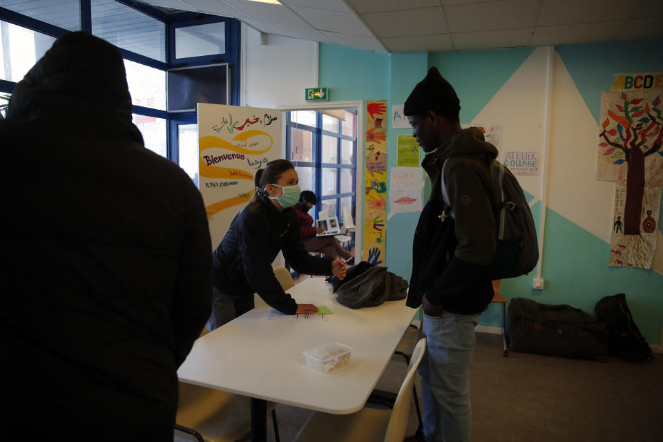 A volunteer helps fill out documents in the "Aurore" center for homeless and migrants in Paris, Thursday, April 2, 2020. Amid the coronavirus lockdown, charity workers at France's Aurore association, are preparing more than a thousand meals a day for migrants and the homeless on the half-abandoned grounds of a former Paris hospital whose patron saint was devoted to the poor. (AP Photo/Francois Mori)