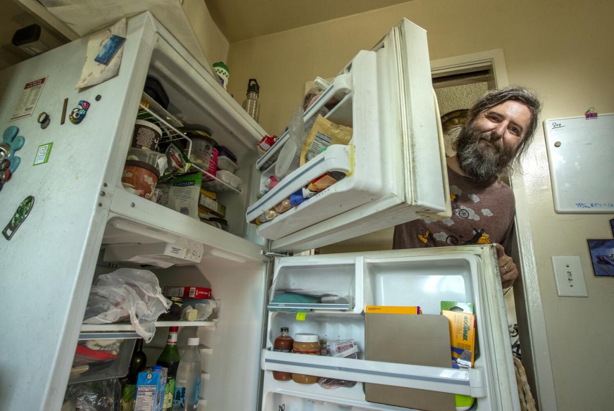 A man holds open his stocked fridge and freezer and smiles