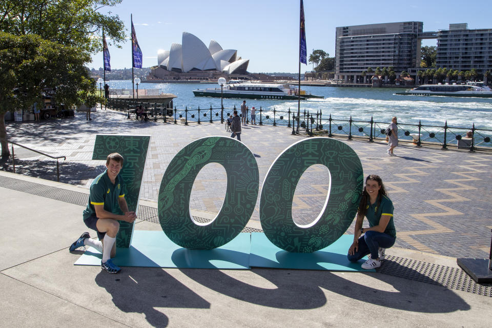 Australian Olympians Edward Fernon, modern pentathlon, and slalom canoeist Jess Fox pose by a sign at a ceremony to mark 100 days before the start of the Tokyo Olympics in Sydney Wednesday, April 14, 2021. Olympics live sites will be held across Australia during the Olympic Games, from July 23 to Aug. 8 2021, taking advantage of the one hour time zone difference for Australians to watch athletes perform. (AP Photo/Mark Baker)