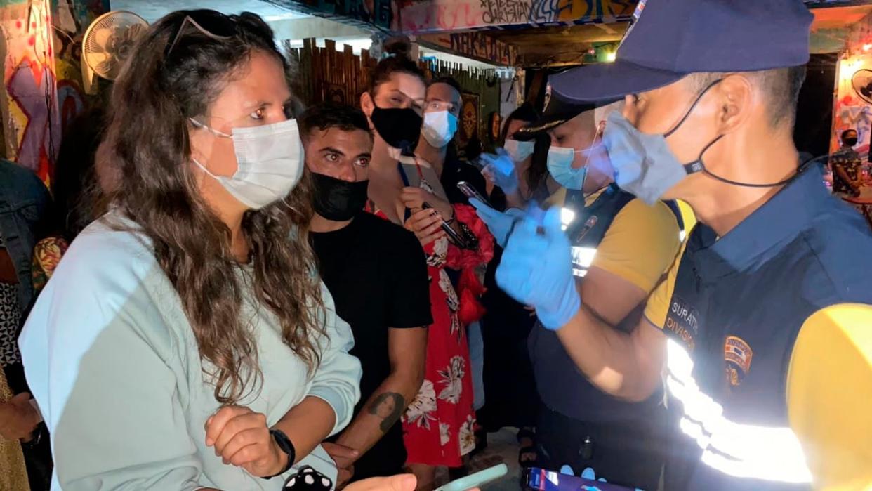 <p>Thai immigration officers talk to people at a bar on Koh Phangan island, southern Thailand, on 26 January</p> (AP)