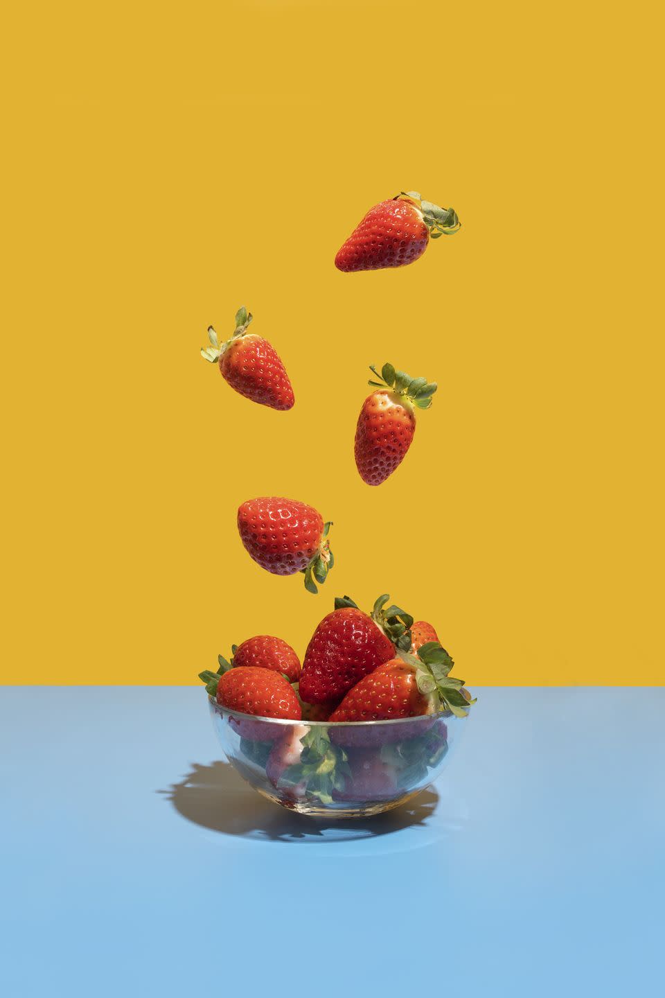 strawberries flying in the bowl on the blue yellow background