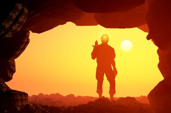 A man standing at the mouth of a mine with the sun behind him