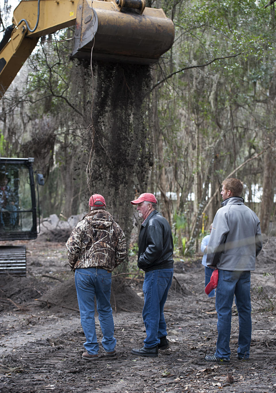 Patrick Sessions, center, and his son Jason, right, watch as Alachua County Sheriffs technicians use a back hoe Thursday, Feb. 2, 2014, in Gainesville, Fla., to dig for evidence in the 1989 disappearance of Tiffany Sessions, a University of Florida student. The sheriffs department announced they have linked the disappearance to Paul Rowles, a serial killer who died in prison last year. (AP Photo/Phil Sandlin)