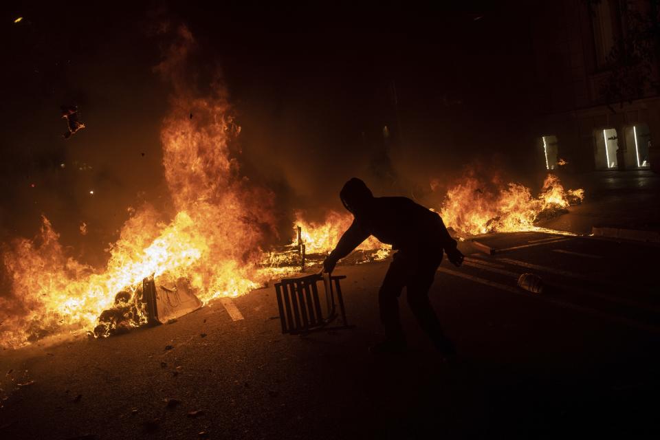 A protester drags a chair next to a burning barricade during clashes with police in Barcelona, Spain, Tuesday, Oct. 15, 2019. Spain's Supreme Court on Monday convicted 12 former Catalan politicians and activists for their roles in a secession bid in 2017, a ruling that immediately inflamed independence supporters in the wealthy northeastern region. (AP Photo/Bernat Armangue)