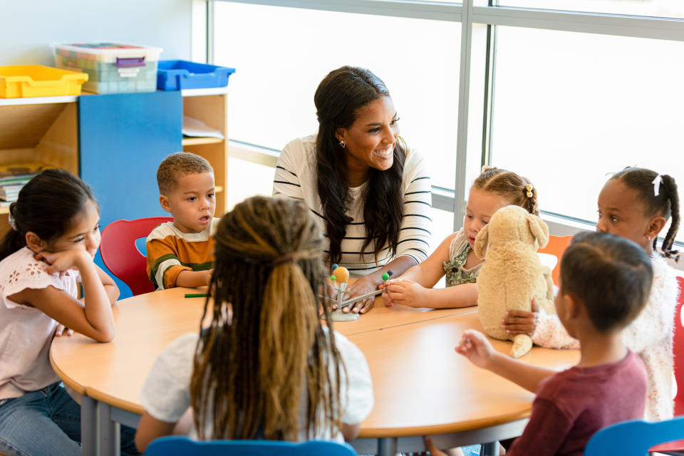 nursery worker sitting at table with a group of nursery age children