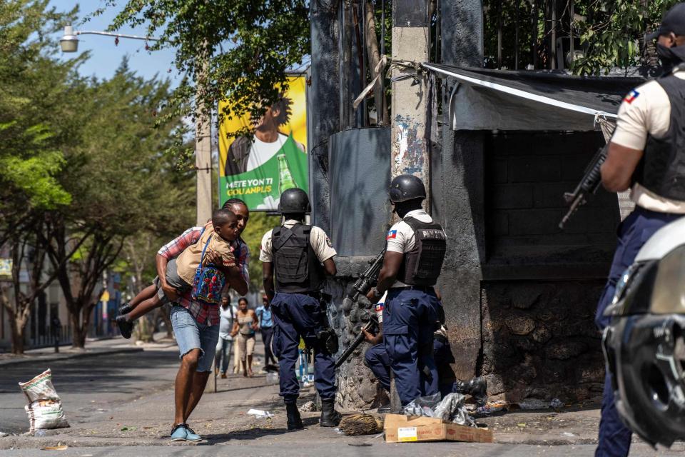 A person carries a child past Haitian National Police attempting to repel gangs in a neighborhood near the Presidential Palace in the center of Port-au-Prince, Haiti on March 3, 2023.