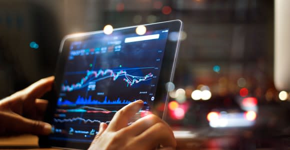 A pair of hands holding a tablet with stock charts on it.