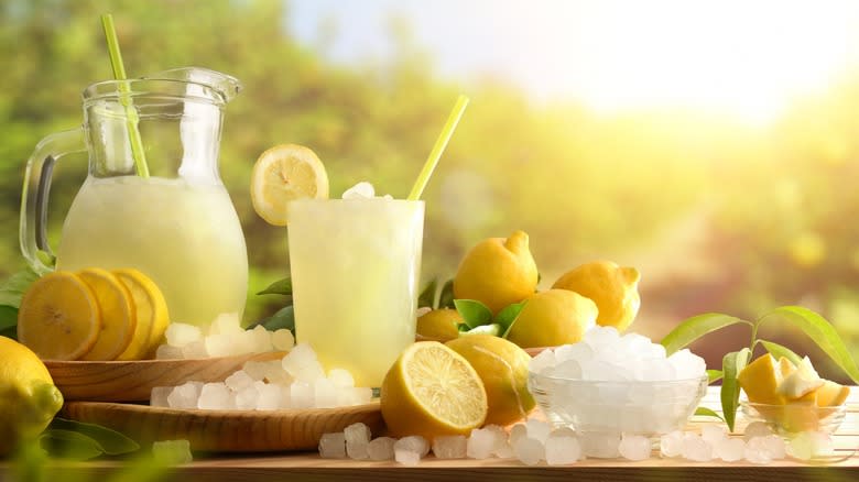 Lemonade pitcher, glass, lemons, and ice on an outdoor table