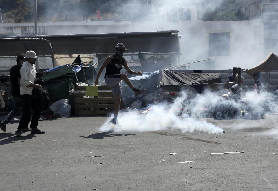 A man kicks a tear gas canister during minor clashes between riot police and migrants near Mytilene town, on the northeastern island of Lesbos, Greece, Saturday, Sept. 12, 2020. Thousands of asylum-seekers spent a fourth night sleeping in the open on the Greek island of Lesbos, after successive fires destroyed the notoriously overcrowded Moria camp during a coronavirus lockdown. (John Liakos/InTime News)