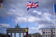 A person raises the Union Jack flag in front of the Brandenburg Gate at the eve of the visit of King Charles III at the German capital, in Berlin, Tuesday, March 28, 2023. Britain's King Charles III and Camilla, the Queen Consort, will make an official visit to Germany from March 29 to 31, 2023. (AP Photo/Markus Schreiber)