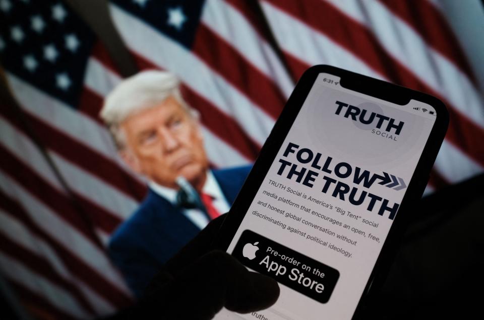 This illustration photo shows a person checking the app store on a smartphone for Truth Social, with a photo of former President Donald Trump on a computer screen in the background, in Los Angeles, Oct. 20, 2021.