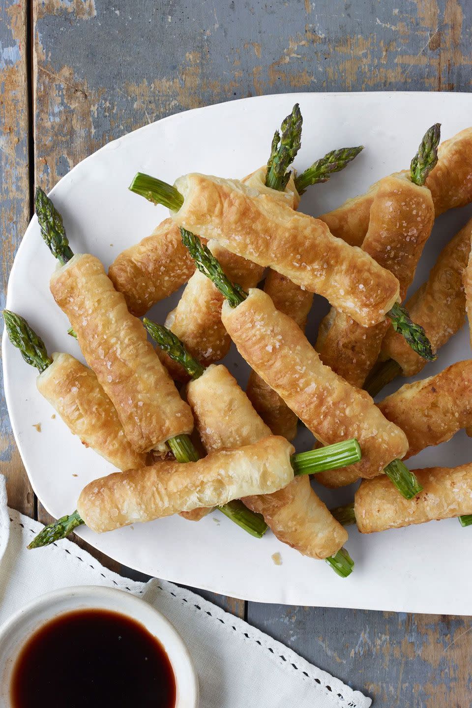 pastry wrapped asparagus with balsamic dipping sauce on a white oval serving platter