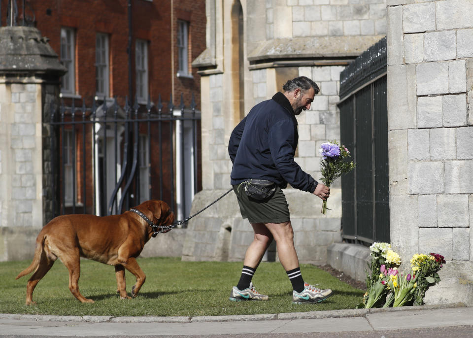 A man lays bunch of flowers in tribute to Prince Philip outside Windsor Castle In Windsor, England, Friday, April 16, 2021. Prince Philip husband of Britain's Queen Elizabeth II died April 9, aged 99, his funeral will take place Saturday at Windsor Castle in St George's Chapel. (AP Photo/Alastair Grant)