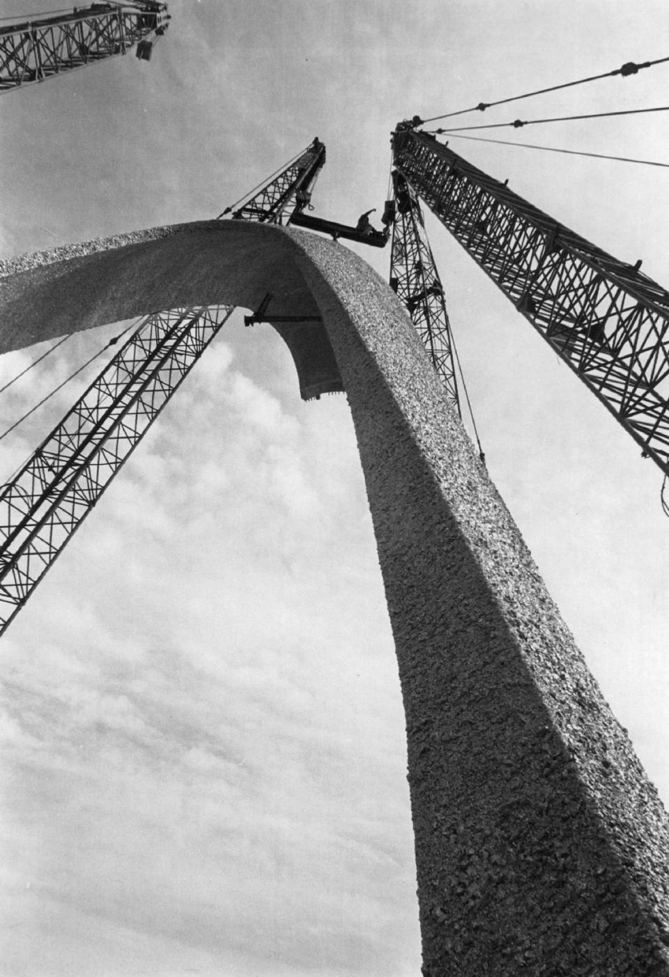 One leg of the giant Arch of Industry at Sunshine State Industrial Park off the Palmetto Expressway towers in the sky after being hoisted by five cranes. The other 100-ton leg followed. Spanning the entrance to the industrial park, the arch was covered with marble chips and gold aluminum flecking to give the appearance of gold.