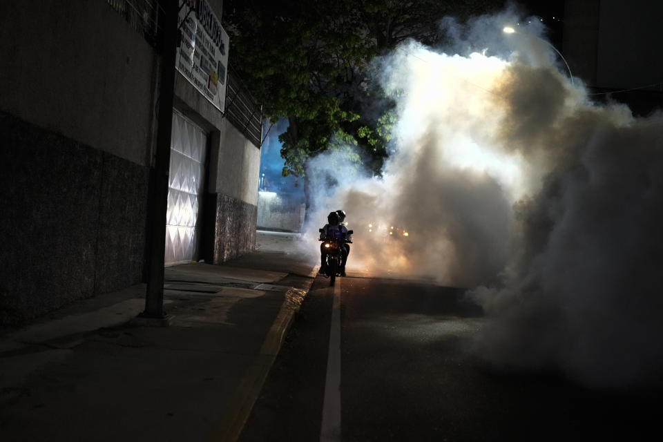 A motorcyclist drives past clouds of insecticide during a fumigation campaign against dengue-promoting mosquitoes, in the Altamira neighborhood of Caracas, Venezuela, Tuesday, Dec. 12, 2023. (AP Photo/Matias Delacroix)
