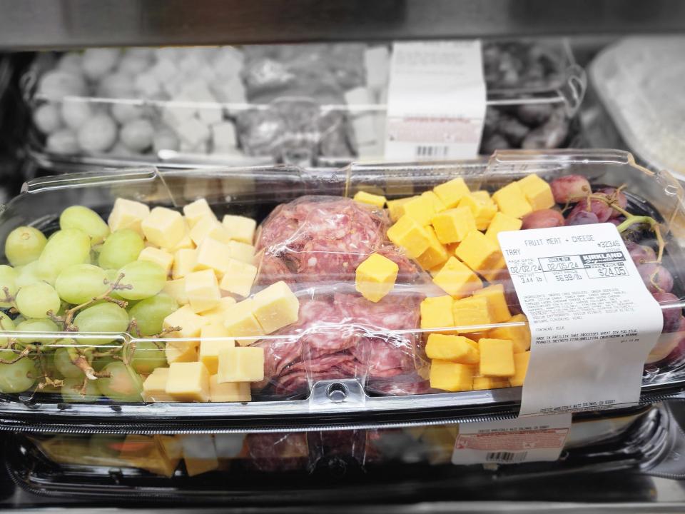 A clear plastic tray containing pieces of salami, cheese cubes, and grapes