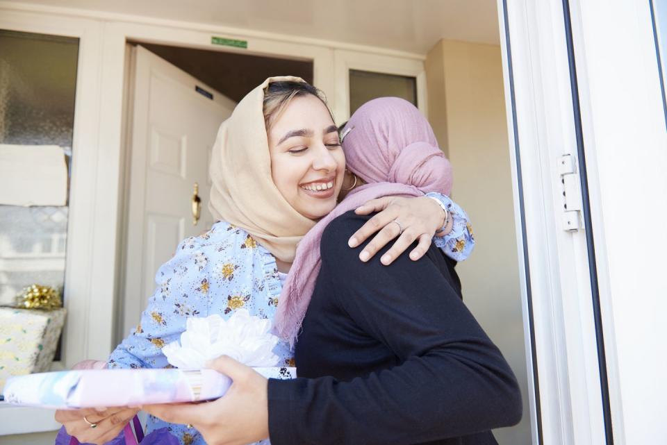 young woman welcomes and hugs a friend holding a gift to eid al fitr celebration