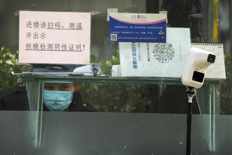 A security guard keeps watch inside a booth displaying a temperature scan device and a travel QR code, outside an office building in Beijing, Monday, Dec. 12, 2022. China will drop a travel tracing requirement as part of an uncertain exit from its strict "zero-COVID" policies that have elicited widespread dissatisfaction. (AP Photo/Andy Wong)