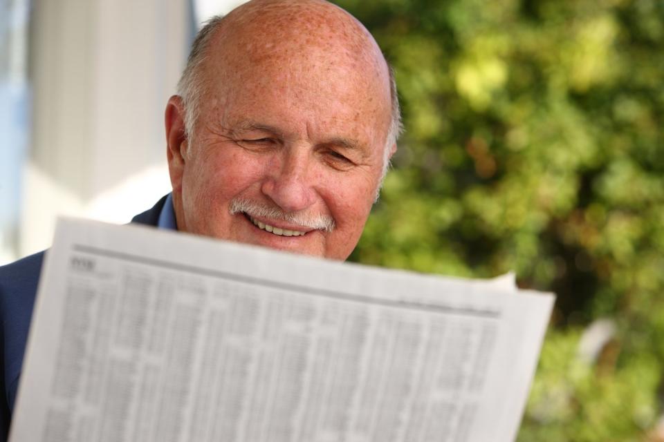 A smiling person reading a financial newspaper while seated outside on a porch.