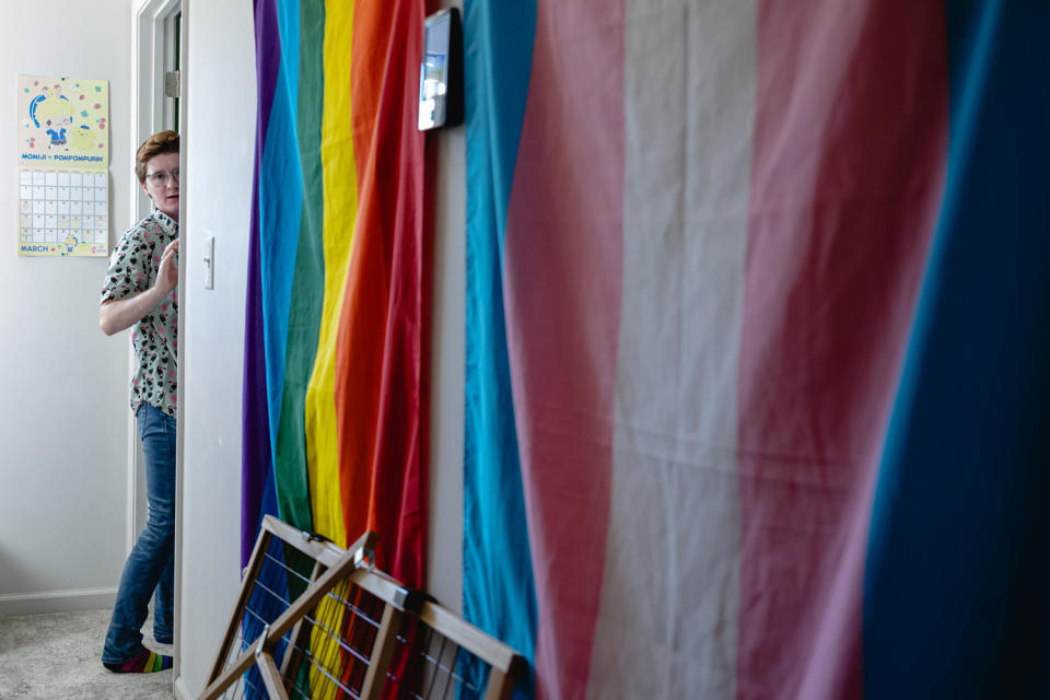 Adrian Whittamore peeks beyond a doorway next to a wall with the pride flag (Jon Cherry for NBC News)