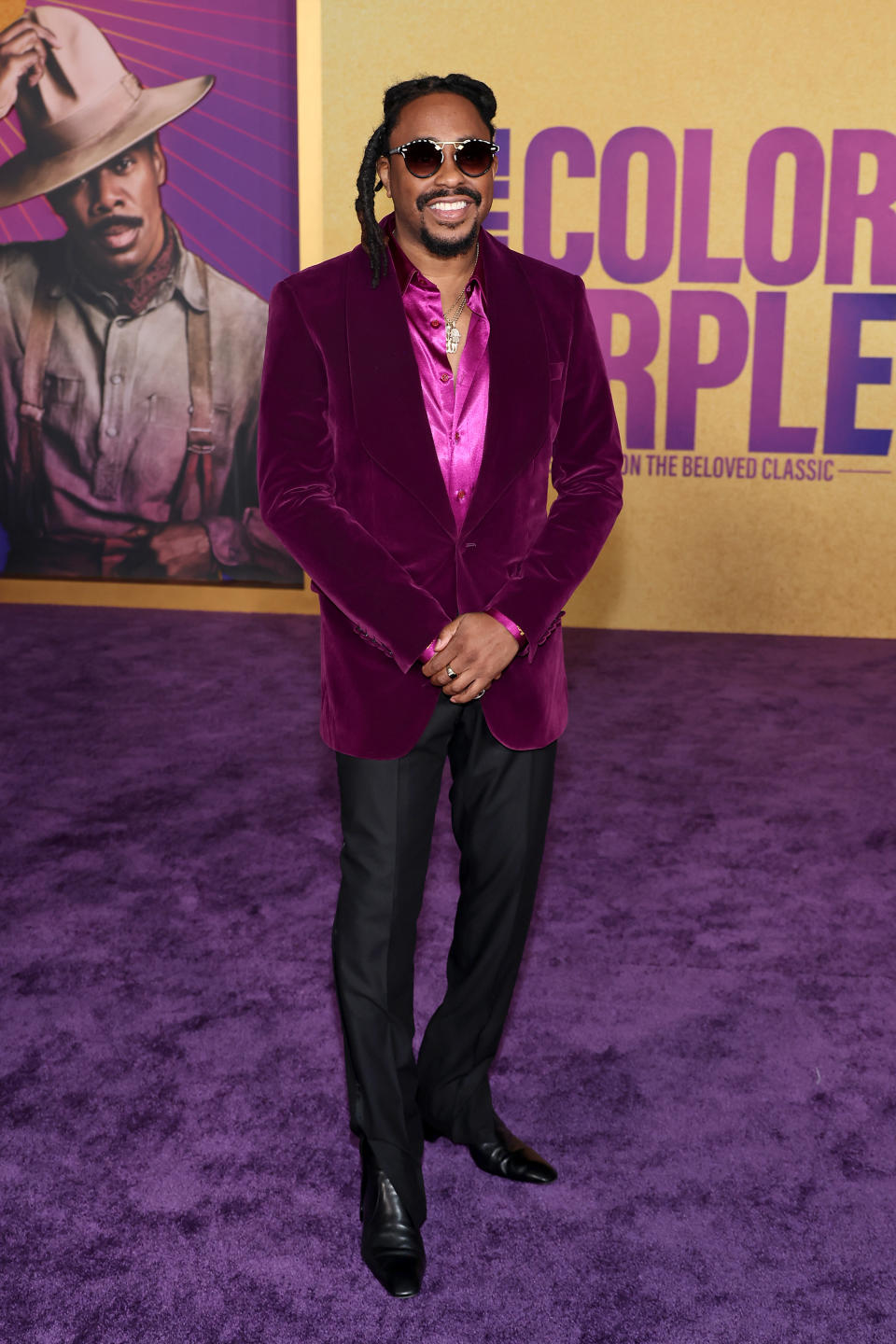 Raheem  in a purple velvet suit jacket, purple shirt, and black pants