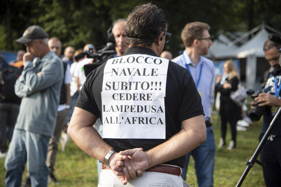 A man wears a sign with writing reading in Italian "Naval blockade immediately!! Give up Lampedusa to Africa" as he attends annual League (Lega) party rally, where French right-wing leader Marine Le Pen talked with Italian Vice Premier Matteo Salvini, in Pontida, northern Italy, Sunday, Sept. 17, 2023. EU Commission President Ursula von der Leyen on Sunday visited with Italian Premier Giorgia Meloni the island of Lampedusa, overwhelmed with nearly 7,000 migrant arrivals in a single day this week. (Claudio Furlan/LaPresse via AP)
