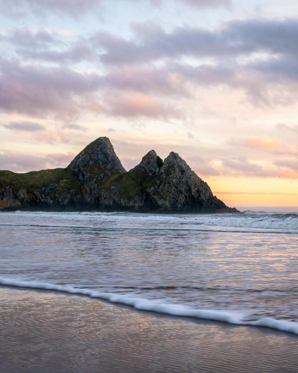 Photo of gentle, milky waves lapping at the beach with the coast in background.