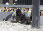 Armed off-duty police officers take cover during and exchange of gunfire with army soldiers, as they protest over police pay and working conditions, in Port-au-Prince, Haiti, Sunday, Feb. 23, 2020. Off-duty police officers and their supporters exchanged fire for nearly two hours with members of the newly reconstituted Haitian army in front of the national palace. (AP Photo/Dieu Nalio Chery)