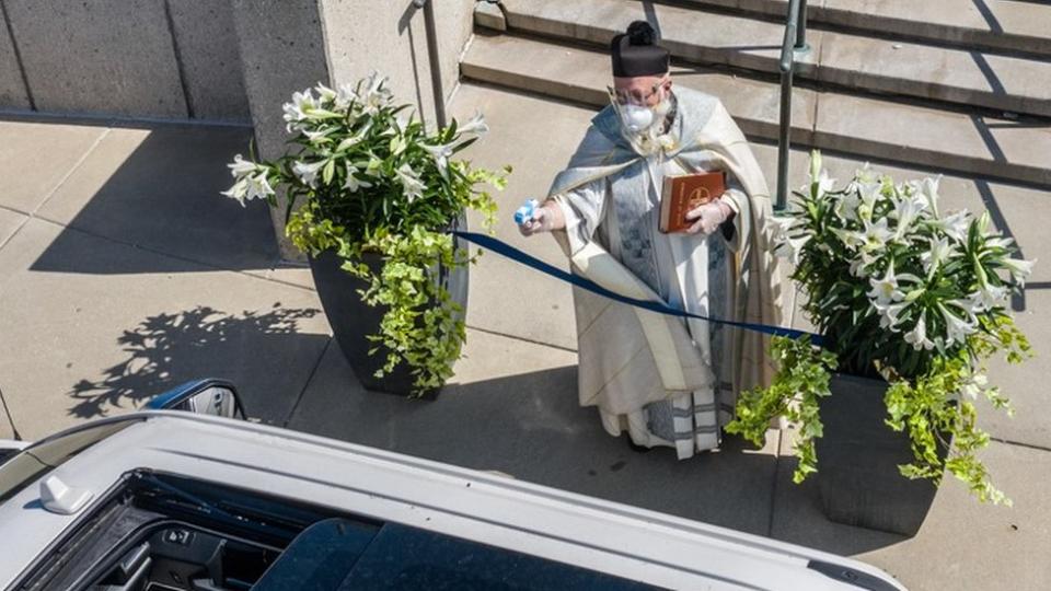 Un sacerdote rocía agua bendita con una pistola de agua.