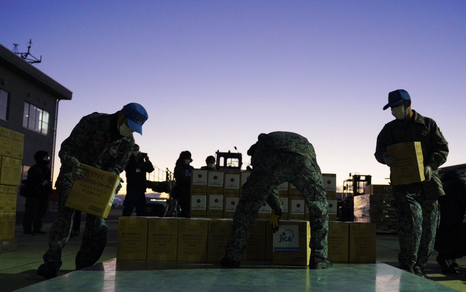 Members of Japan's Air Self-Defense Force help load boxes of water into an airplane at an airbase in Komaki, central Japan, Thursday, Jan. 20, 2022, as they were preparing to take off for Australia on their way to Tonga to transport the emergency relief goods, following Saturday's volcanic eruption near the Pacific nation. Japan's Defense Ministry said it would send emergency relief, including drinking water and equipment for cleaning away volcanic ash. (Kyodo News via AP)