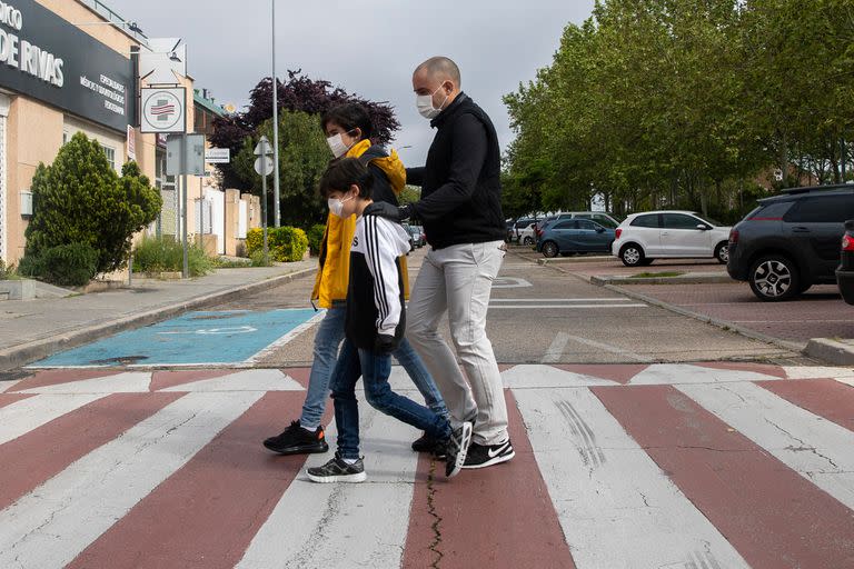 Una familia que usan mascarillas en un cruce peatonal en Rivas Vaciamadrid, España, España, el domingo 26 de abril de 2020. El domingo, los niños menores de 14 años podrán caminar con sus padres hasta por una hora y dentro de un kilómetro de casa , terminando seis semanas de reclusión.