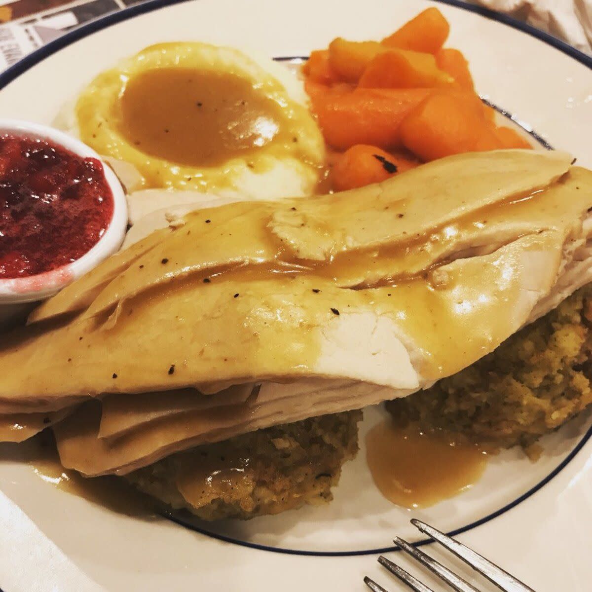 Closeup of Bob Evans Turkey and Gravy Dinner with gravy, stuffing, mashed potatoes, cranberries, and carrots on a blue-lined white plate at Bob Evans