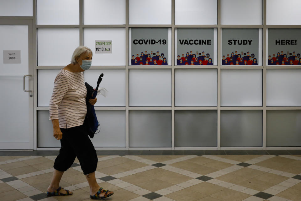 A person wearing a face mask walks in a hallway where signs read "COVID-19 vaccine study here!"