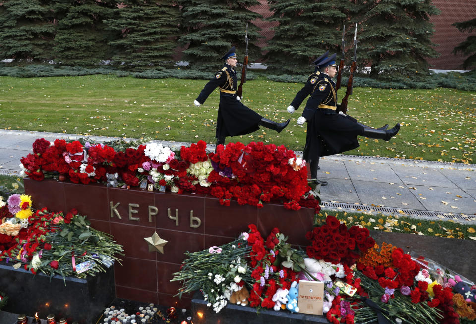 The Kremlin guards march past candles and flowers placed in memory of the victims of Wednesday's attack on a vocational college in Kerch, Crimea, at the memorial stone with the word Kerch in the Alexander Garden near the Kremlin, Moscow, Russia, Thursday, Oct. 18, 2018. A top official in Crimea says authorities are searching for a possible accomplice of the student whose shooting-and-bomb attack on his vocational school killed 20 people and wounded more than 50 others. (AP Photo/Pavel Golovkin)