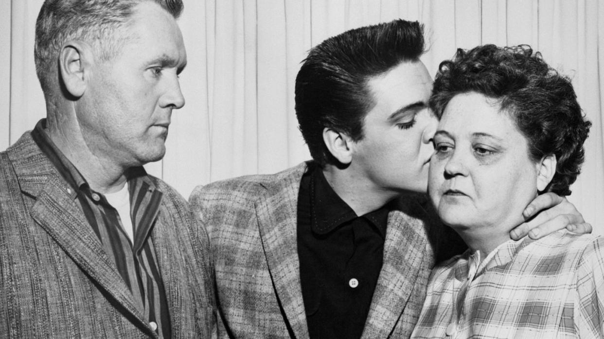 a black and white photo of elvis presley standing with his father and kissing his mother