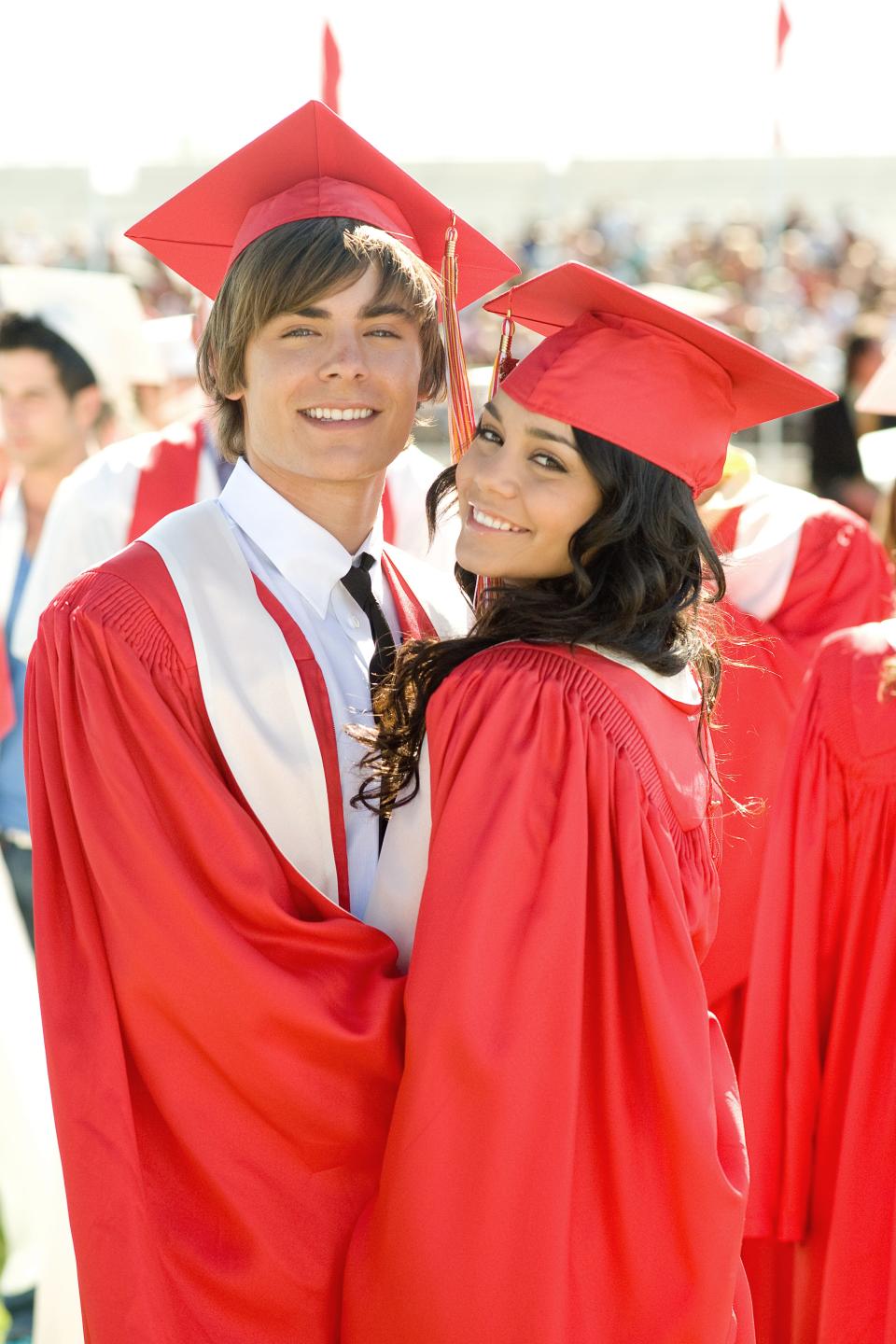 Zac Efron and Vanessa Hudgens are smiling and wearing graduation caps and gowns at a graduation event