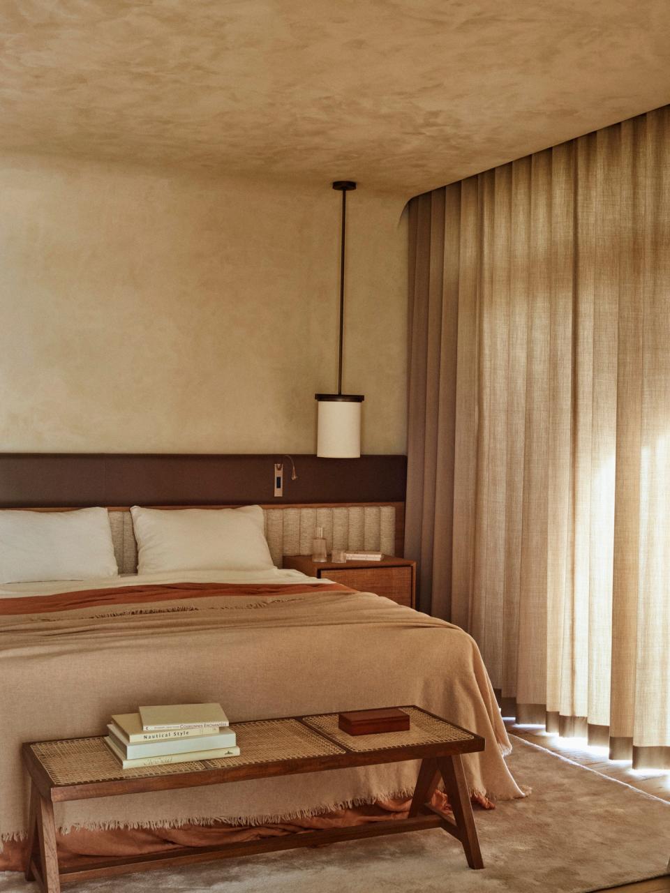 The primary bedroom features a headboard and nightstands by Caprini & Pellerin Architectes and a brass reading light by Meljac. The vintage Chandigarh bench is by Le Corbusier and Pierre Jeanneret. The curtains are Pierre Frey.