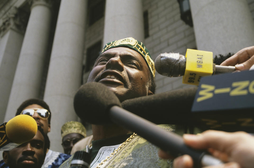 Leonard Jeffries, in characteristic African dress with pillbox hat, addresses the outstretched microphones of reporters.