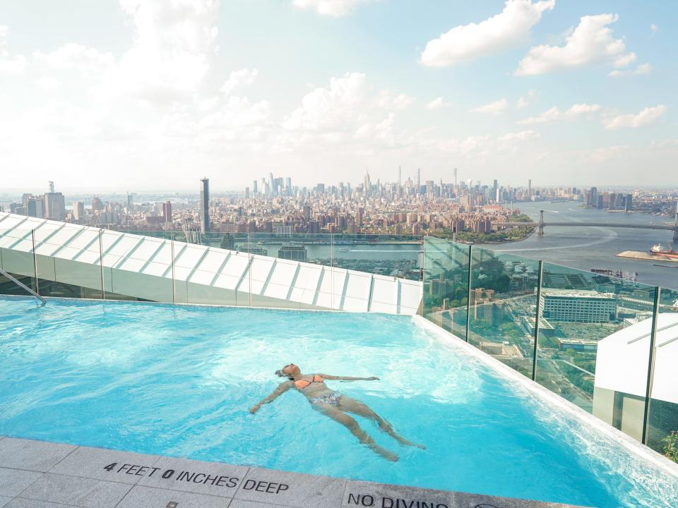 The author floats in the pool with the NYC skyline in the background.
