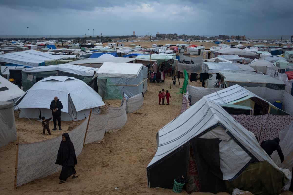 Palestinians displaced by the Israeli air and ground offensive on the Gaza Strip walk through a makeshift tent camp in Rafah (AP)