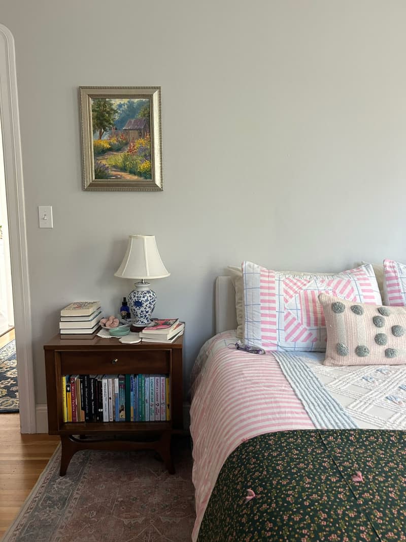 Book filled nightstand next to patterned bedding in cozy bedroom.