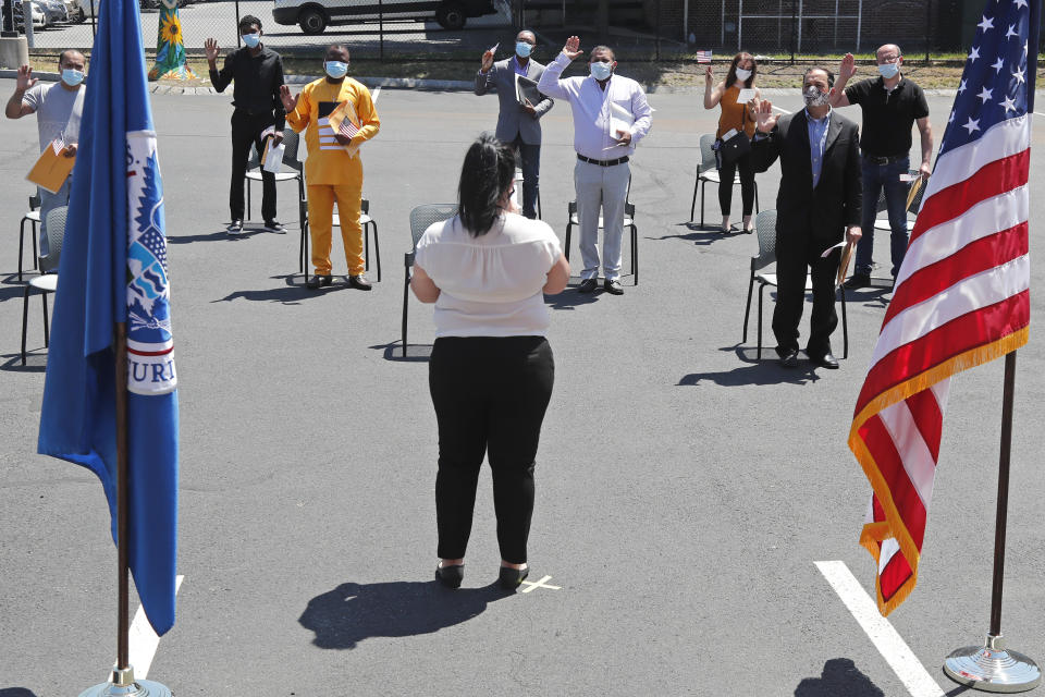 New citizens are sworn in while observing social distancing, outside the U.S. Citizenship and Immigration Services building, Thursday, June 4, 2020, in Lawrence, Mass. The federal agency is resuming services in many cities across the country after being shuttered for more than two months because of the coronavirus pandemic. (AP Photo/Elise Amendola)