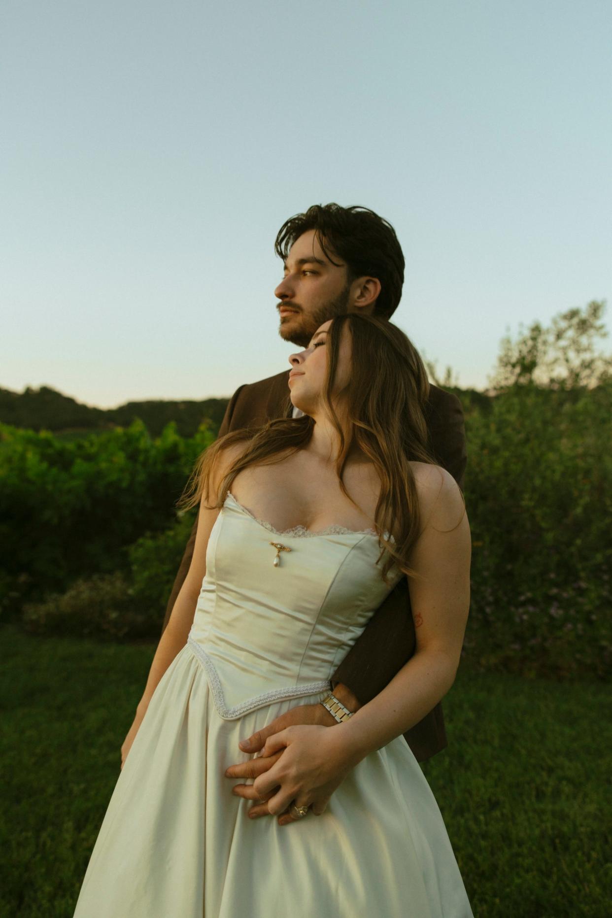 A bride leaning back on her groom in a field.