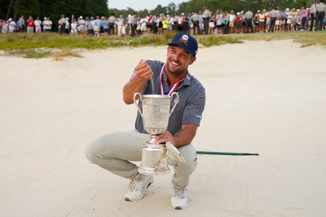 Bryson DeChambeau holds the US Open trophy in a bunker