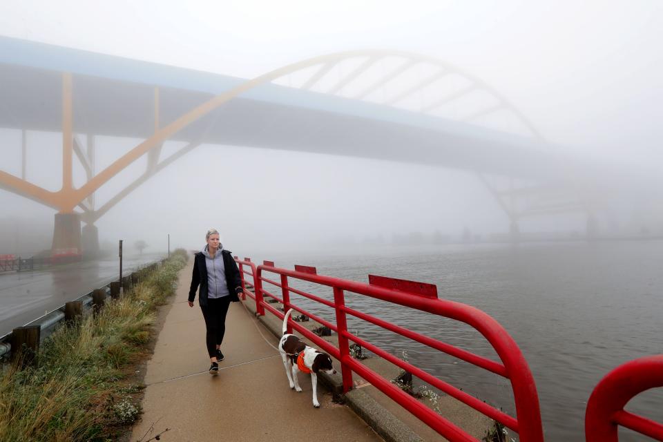 Angie Raasch of Milwaukee walks through the fog with her dog, Remy, a 6-year-old pointer mix rescue dog, along the Kinnickinnic River on the Hank Aaron State Trail near the Hoan Bridge in Milwaukee on Sept. 30, 2019.