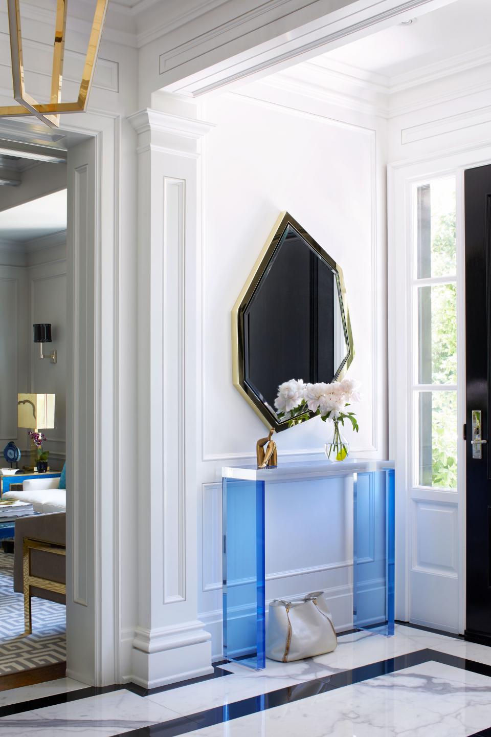 An asymmetrical brass mirror and transparent blue Lucite console make a modern statement against the entryway’s classic black-and-white marble floors. “Each room is very different, yet the spaces transition so beautifully from one to the next,” Hepfer says.