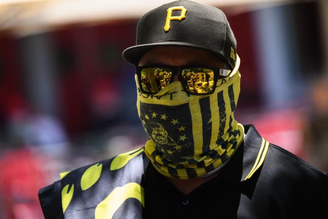 A protester with face covered in a yellow and black neck covering, reflective yellow sunglasses and a black baseball cap marked with a yellow P.